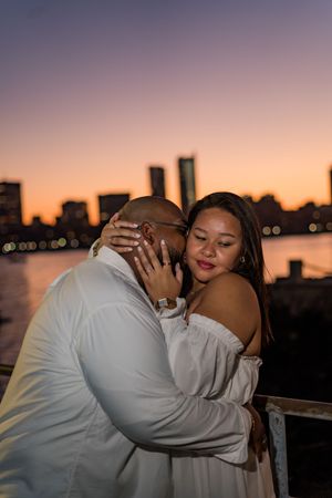 A romantic moment between a couple during golden hour with a city skyline silhouetted in the background.