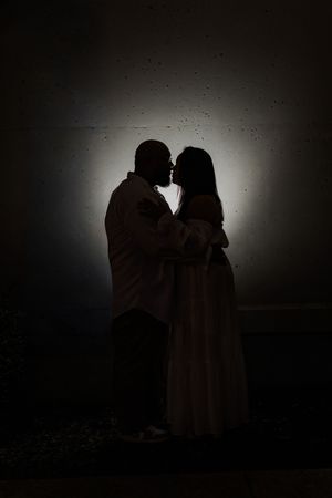 A silhouetted couple embraces in front of a hazy backlit background creating a romantic atmospheric mood.