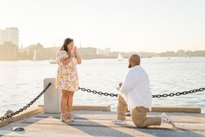 A romantic proposal scene unfolds on a waterfront pier during golden hour as two people share a special moment.