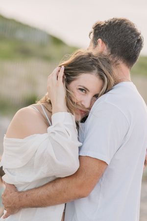 A couple embraces tenderly outdoors with soft lighting as she rests her head against his shoulder.