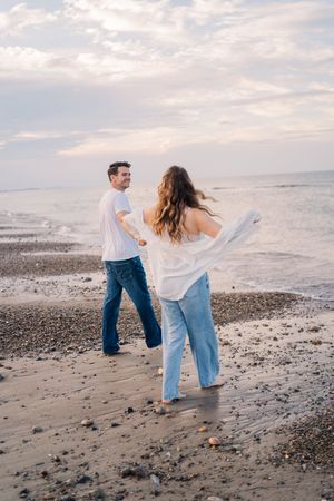Playful couple walking and dancing together on a rocky beach at sunset.