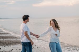 A couple holding hands and sharing a playful moment while walking on a beach at sunset.