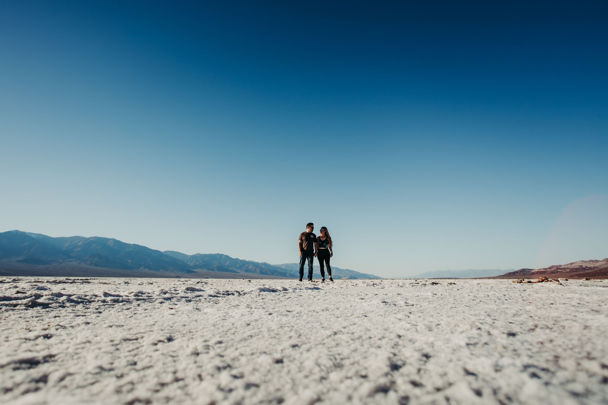 Vast white salt flats landscape stretching to distant mountains under bright blue sky.