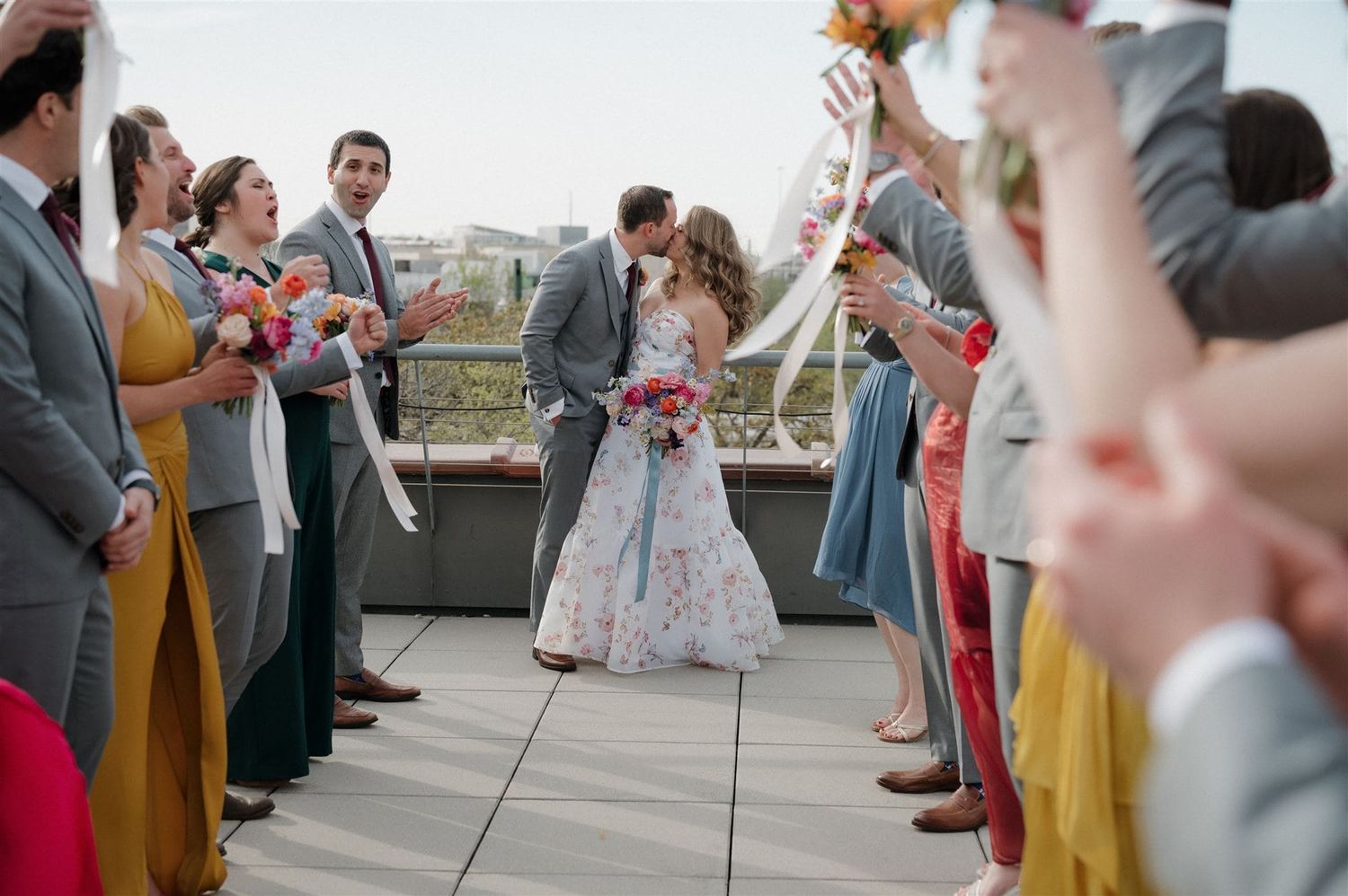 Wedding guests line up outdoors on a rooftop patio to celebrate with a couple during their special moment.