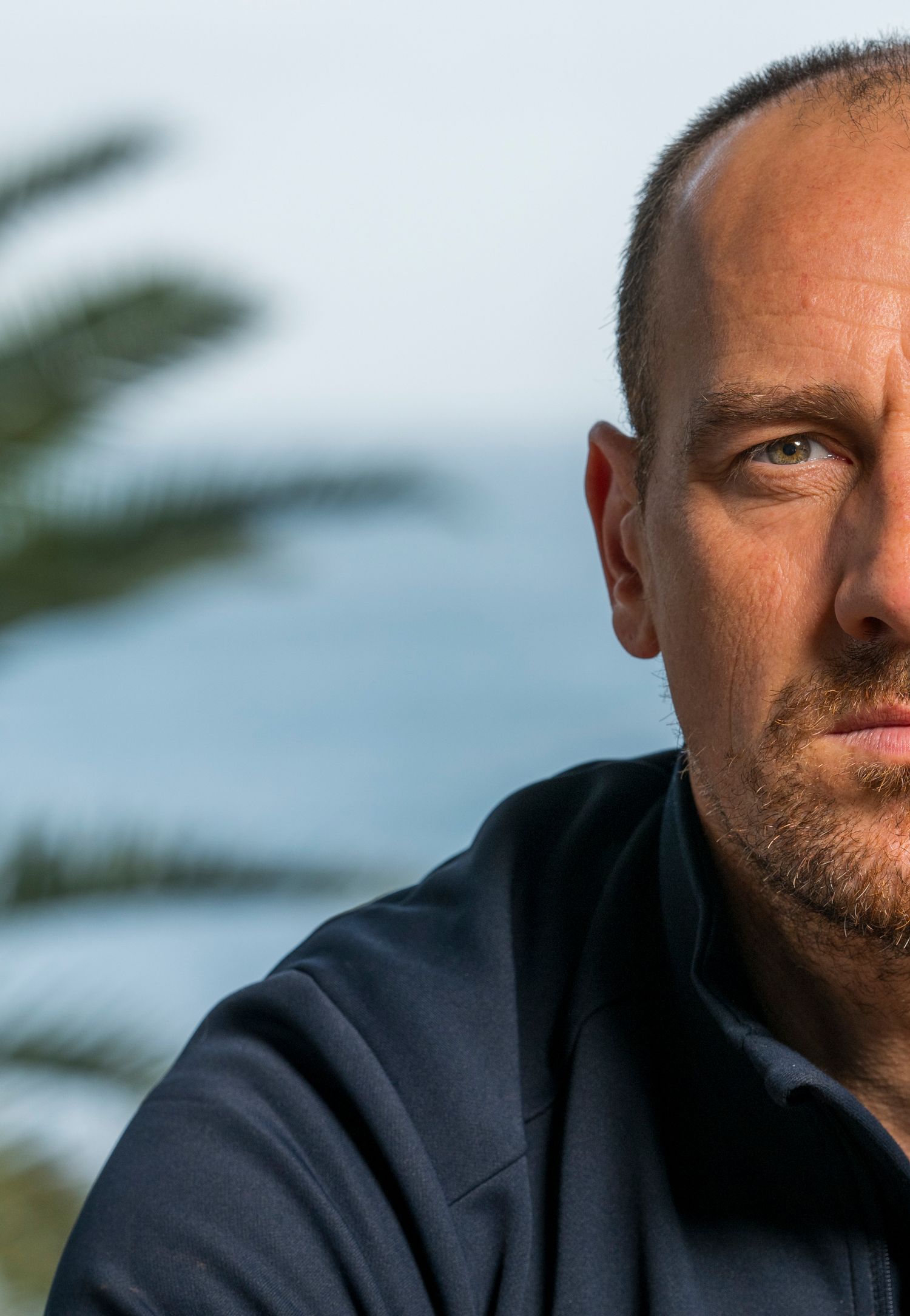 Close-up portrait shot with palm leaves in soft focus background.