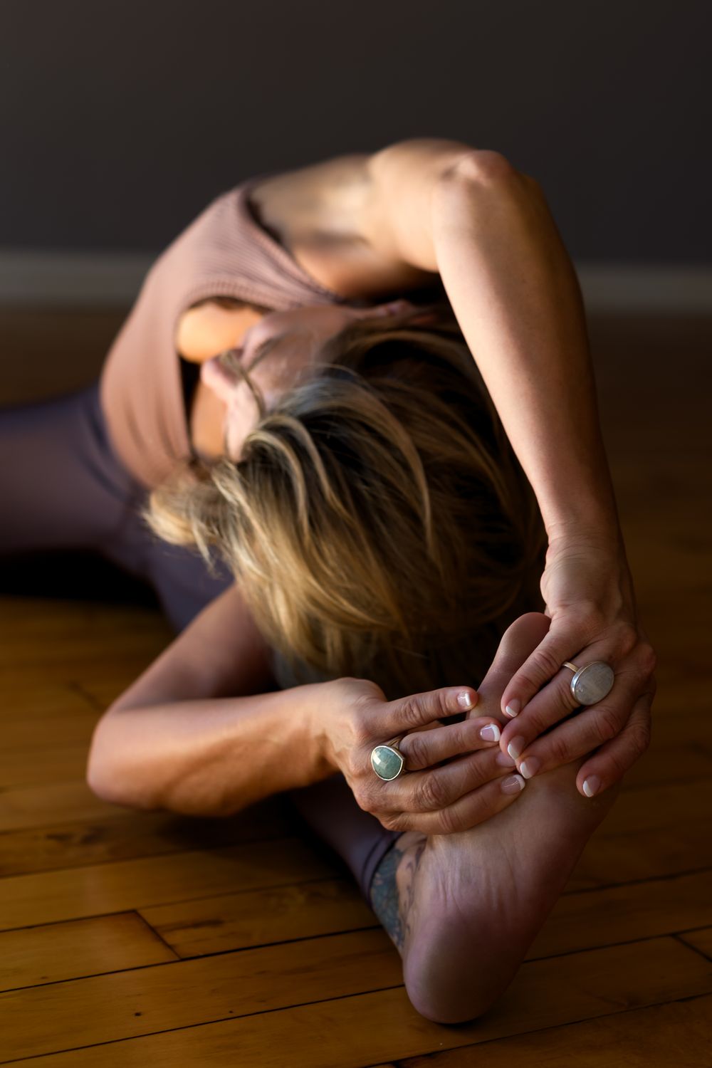 Artistic yoga pose captured in moody lighting on wooden floor.