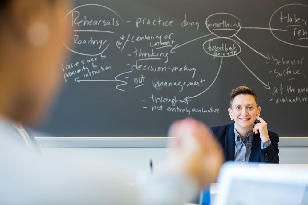 Professor writing mathematical equations and formulas on a large blackboard during a lecture.