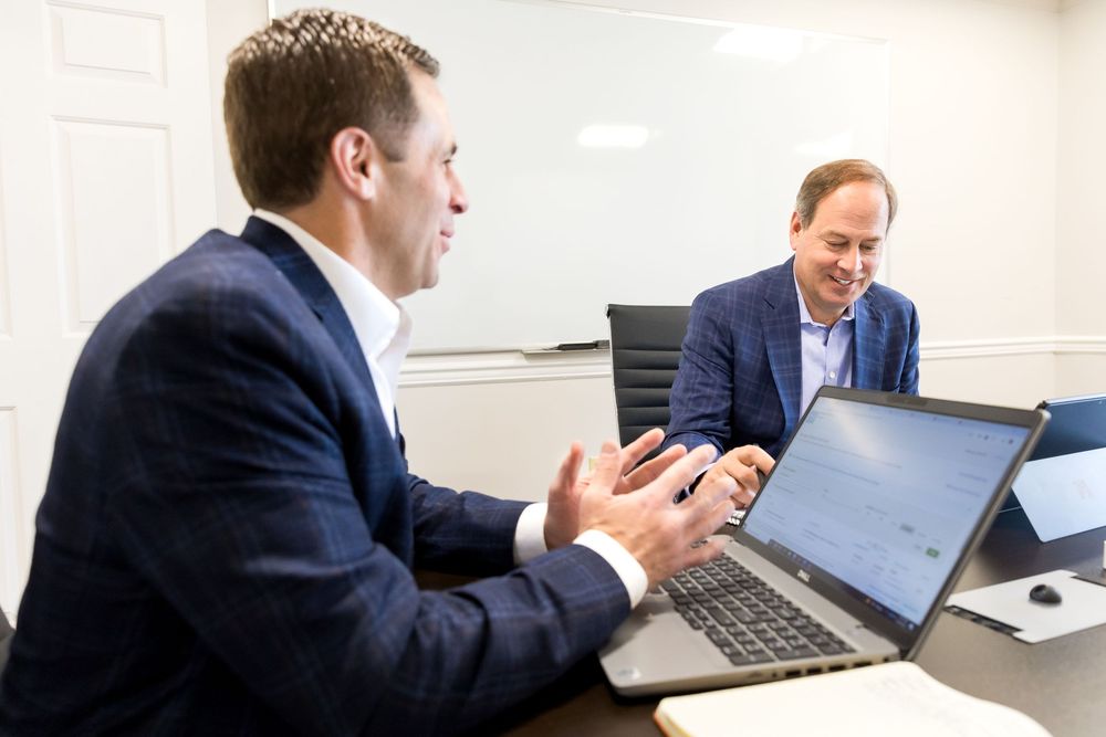 Business professionals in suits collaborate during a meeting while working on laptops in a conference room.
