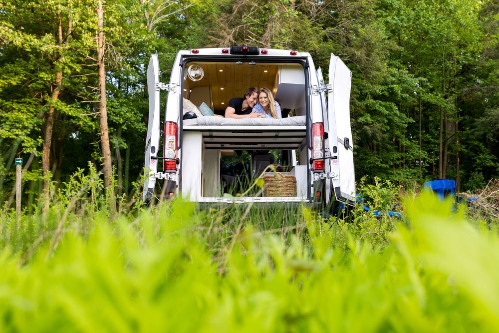 White food truck parked in a lush green summer setting serving customers.