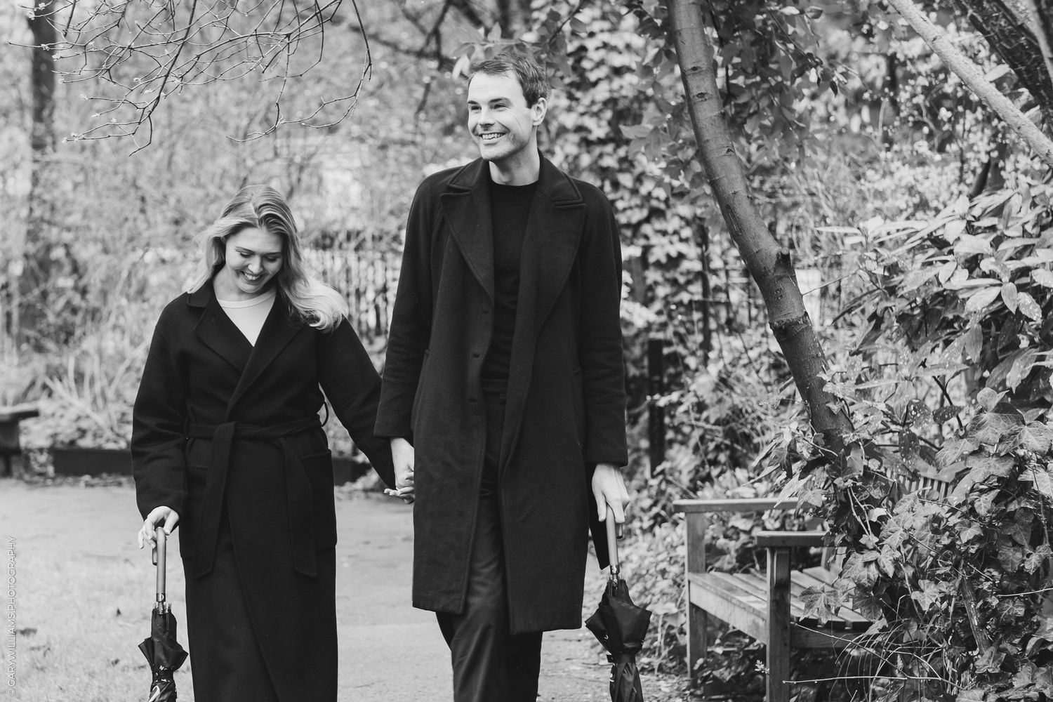 Man and woman in black outfits walking outside in a park in London holding hands