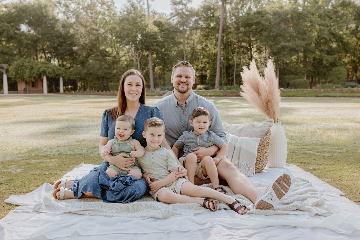 Family group sits together on white blanket for outdoor portrait session.