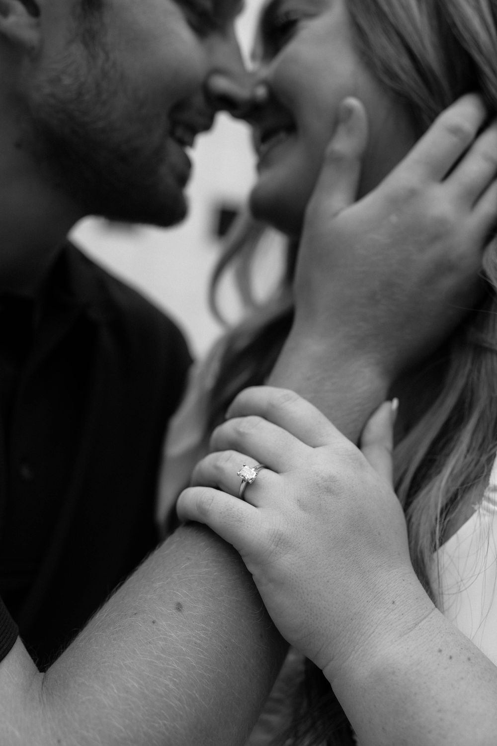Black and white romantic close-up photo showing a tender intimate moment between a couple with an engagement ring visible.