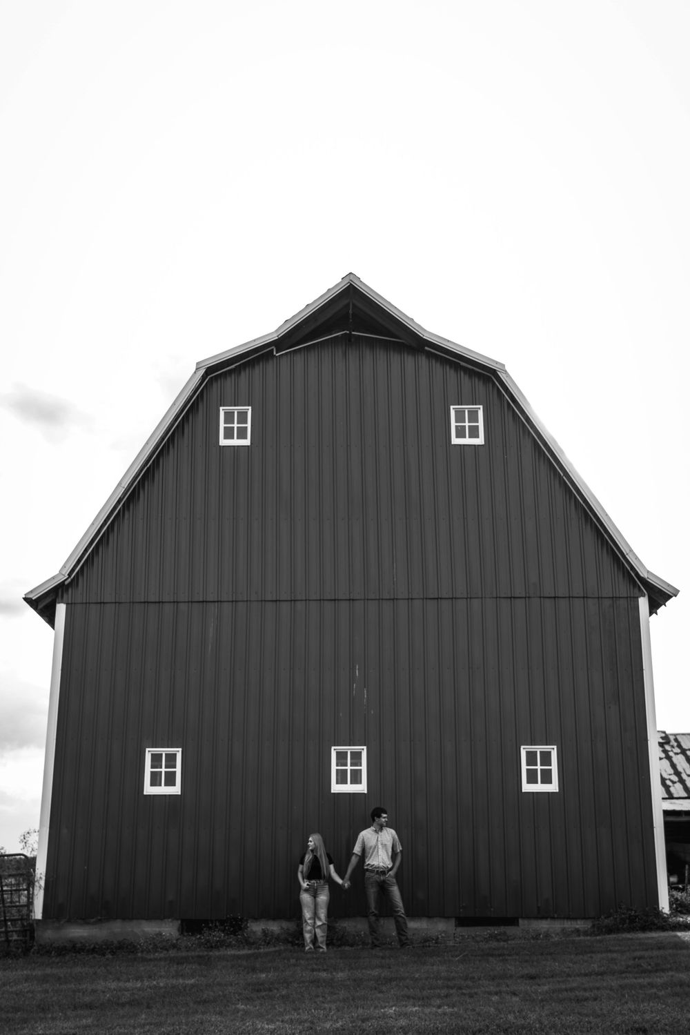 Silhouetted couple standing against large black barn with white windows.