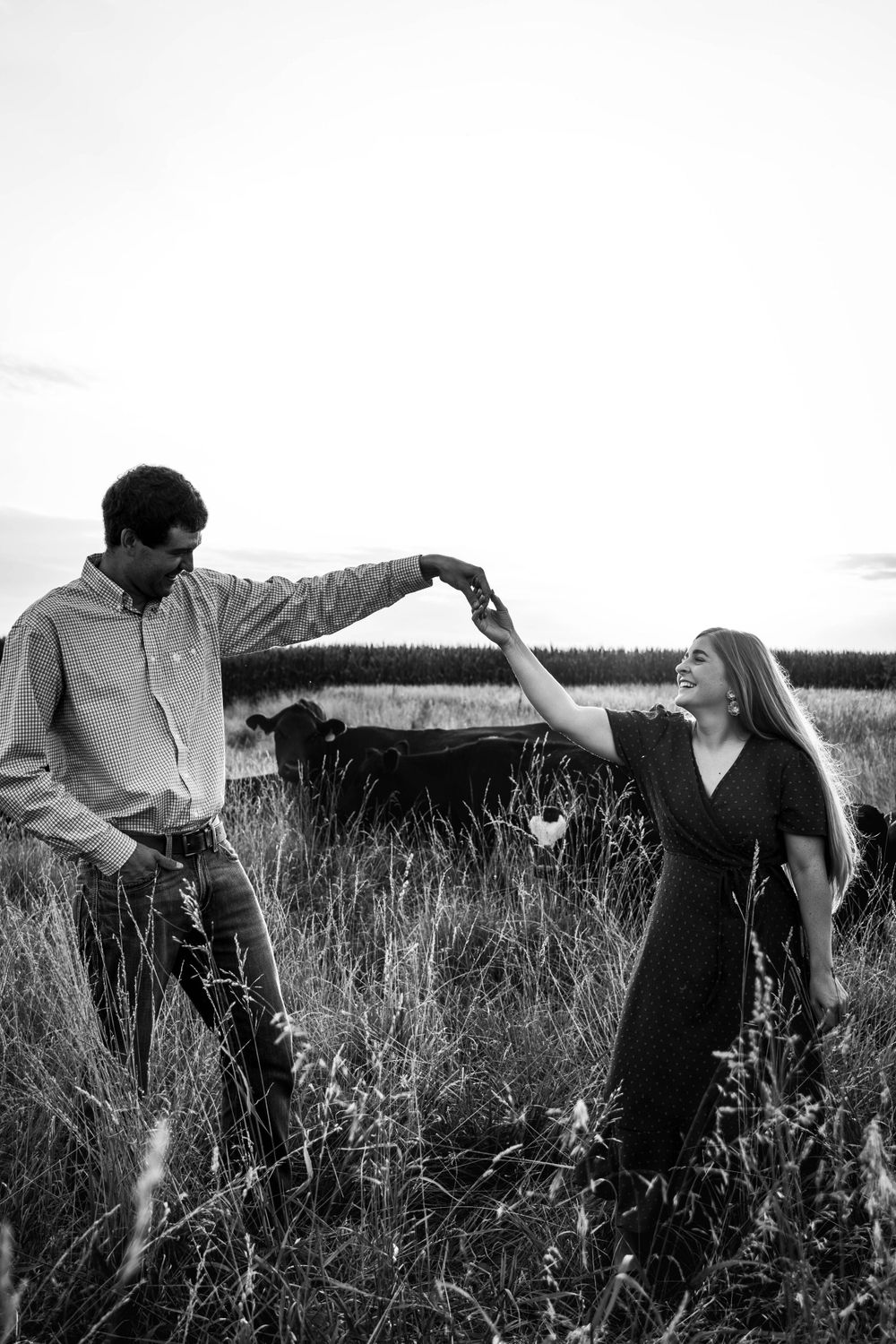 Playful black and white photo of couple dancing in a rustic field at sunset.