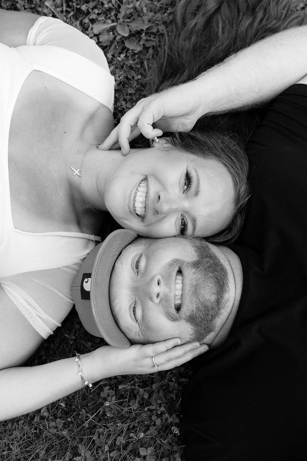 A couple lying on grass in black and white smiling affectionately while looking at the camera.