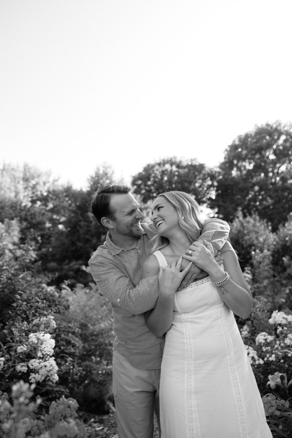 Black and white photo of a happy couple embracing and laughing together in a lush garden setting.