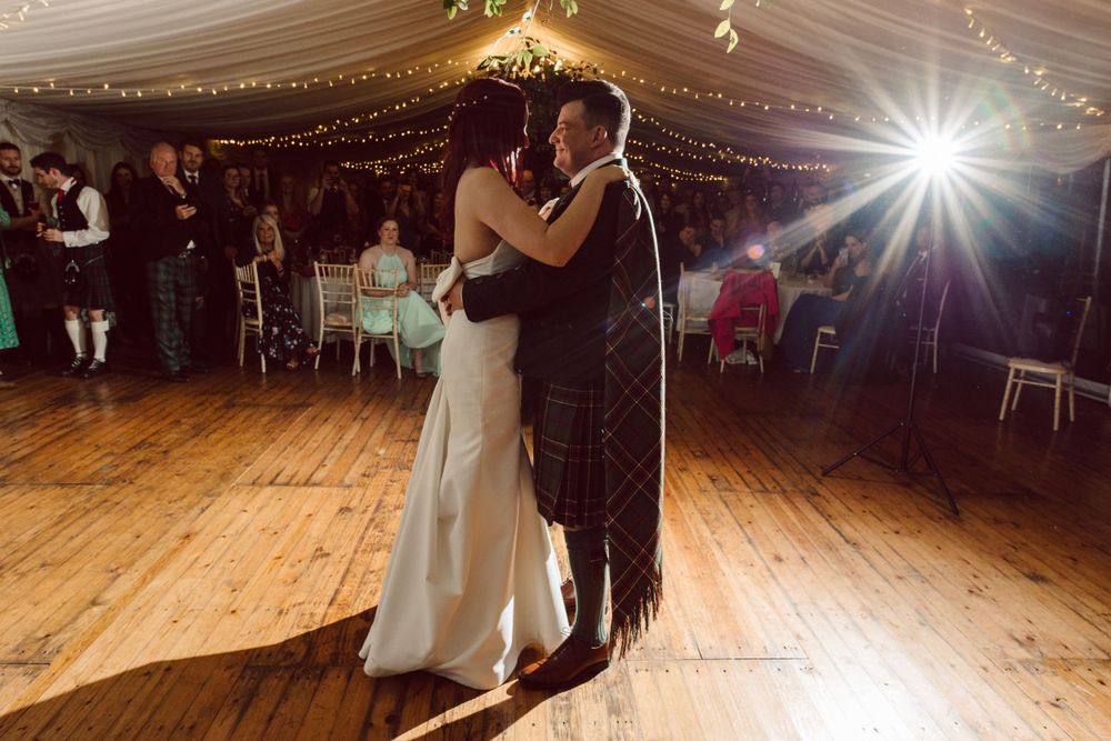 Couples dancing at an elegant wedding reception under draped fabric ceiling with sparkling lights.