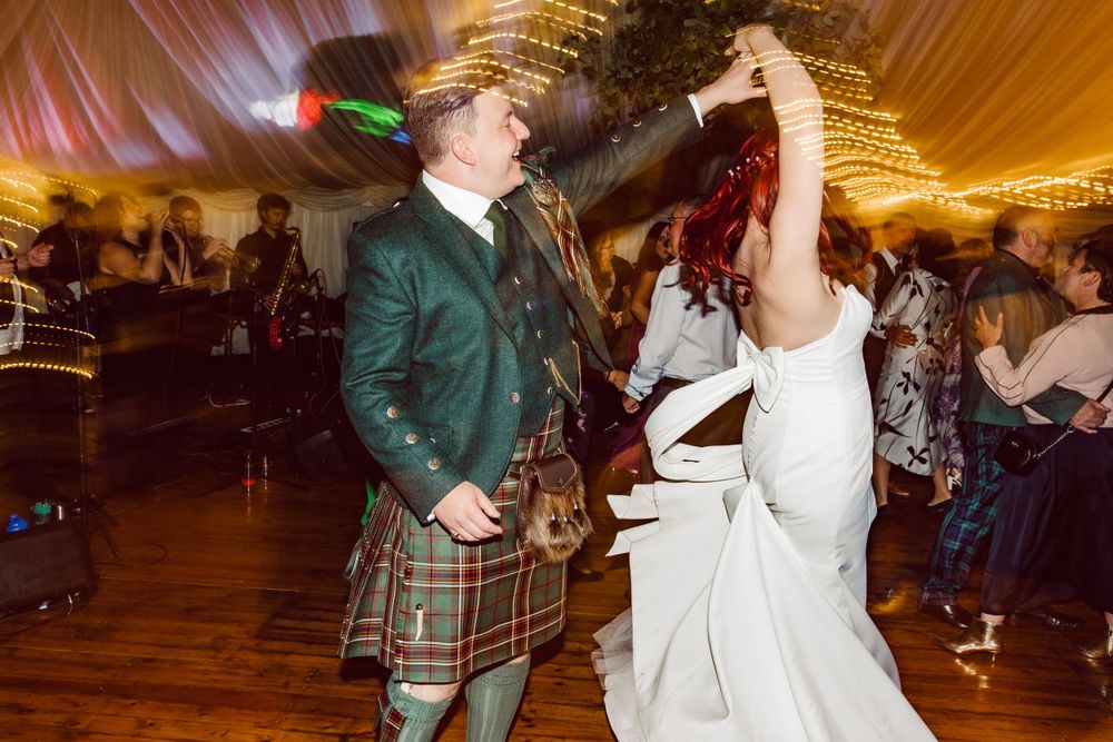 Couples dancing at a wedding reception with traditional Scottish kilts and white gowns.