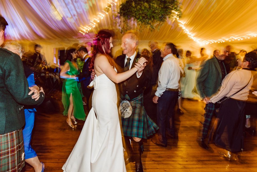 Wedding celebration in a draped tent venue with Scottish kilts and formal attire on the dance floor.