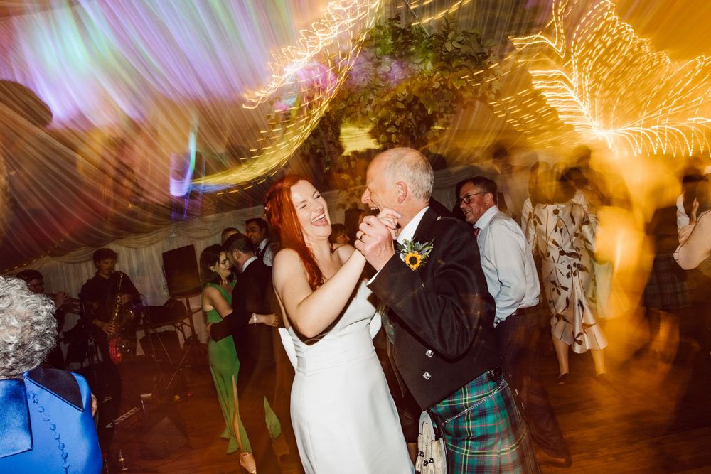 Lively dancing at a wedding reception under warm lighting and draped fabric ceiling.