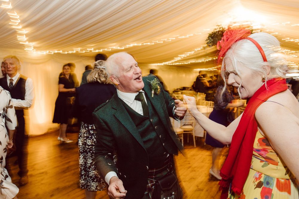 Joyful dancing celebration at a Scottish wedding reception with traditional formal wear.