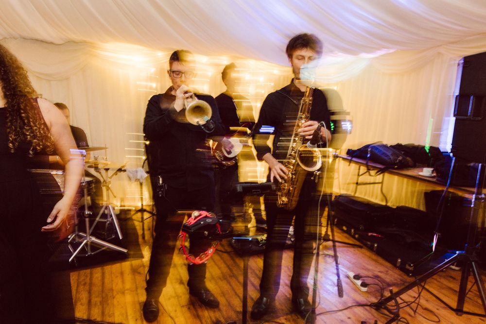 Musicians performing on stage with dramatic lighting and white drapes in the background.