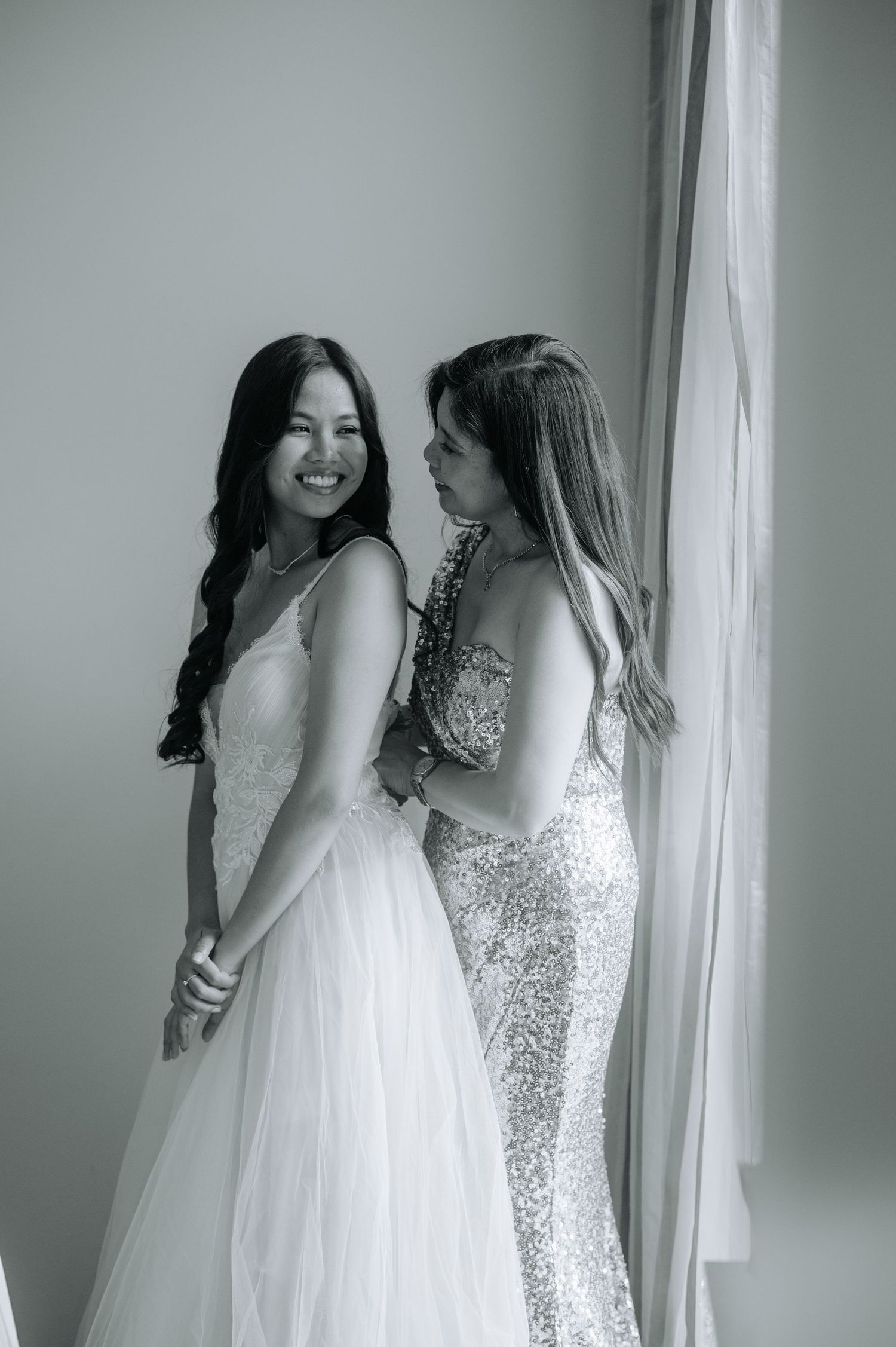 Two people in formal attire sharing a joyful moment by a window.