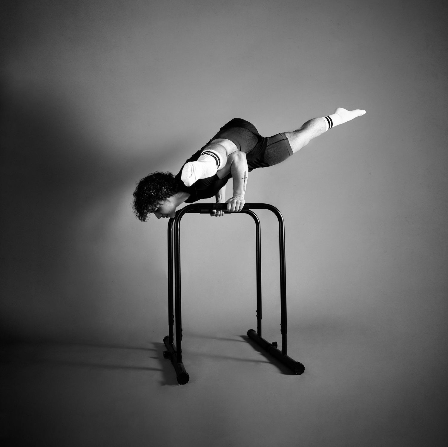 Athlete performing a horizontal hold on parallel bars in dramatic black and white photography against plain background.
