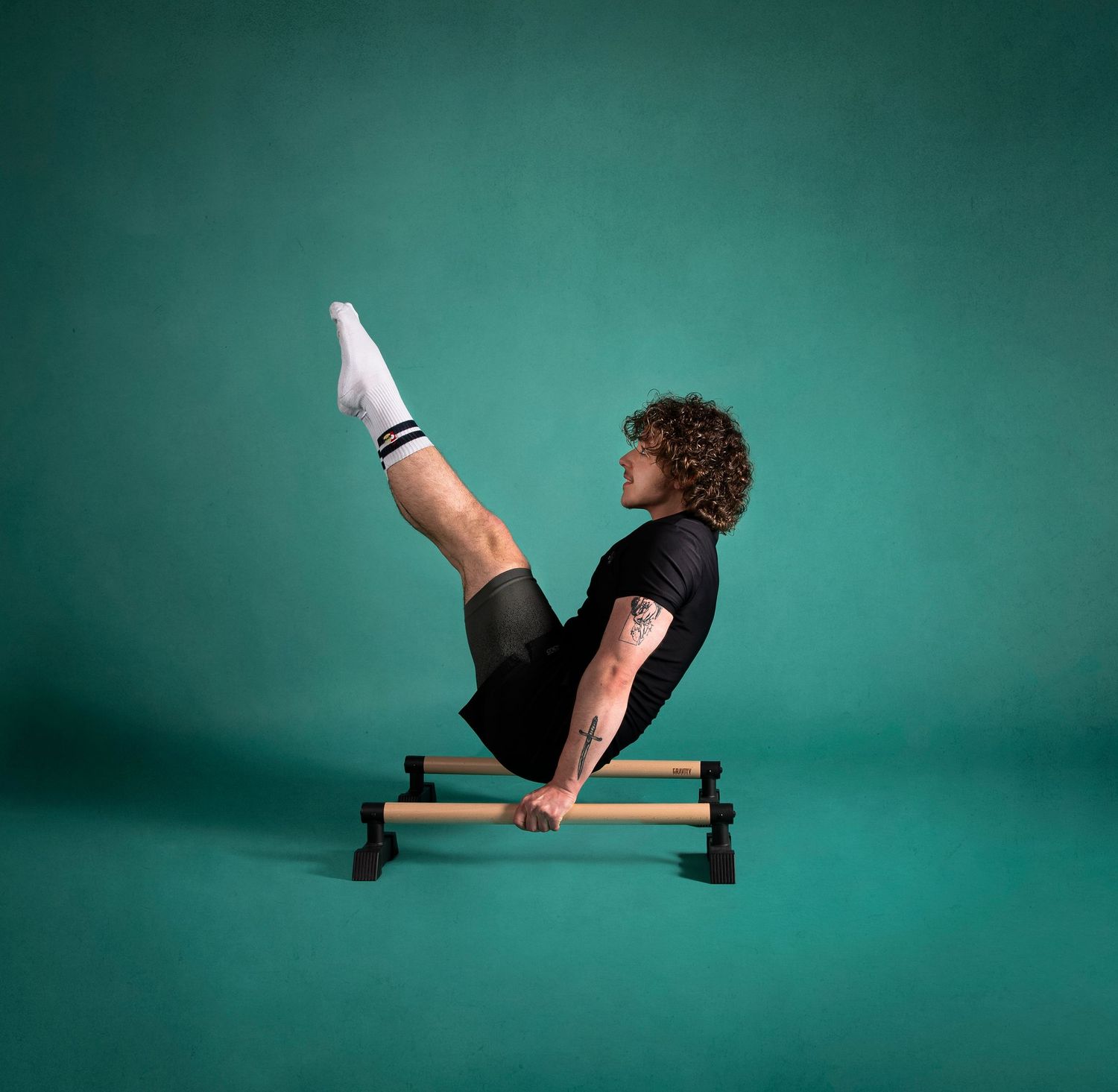 Athletic person performs a challenging L-sit position on parallel bars against turquoise background in a studio setting.