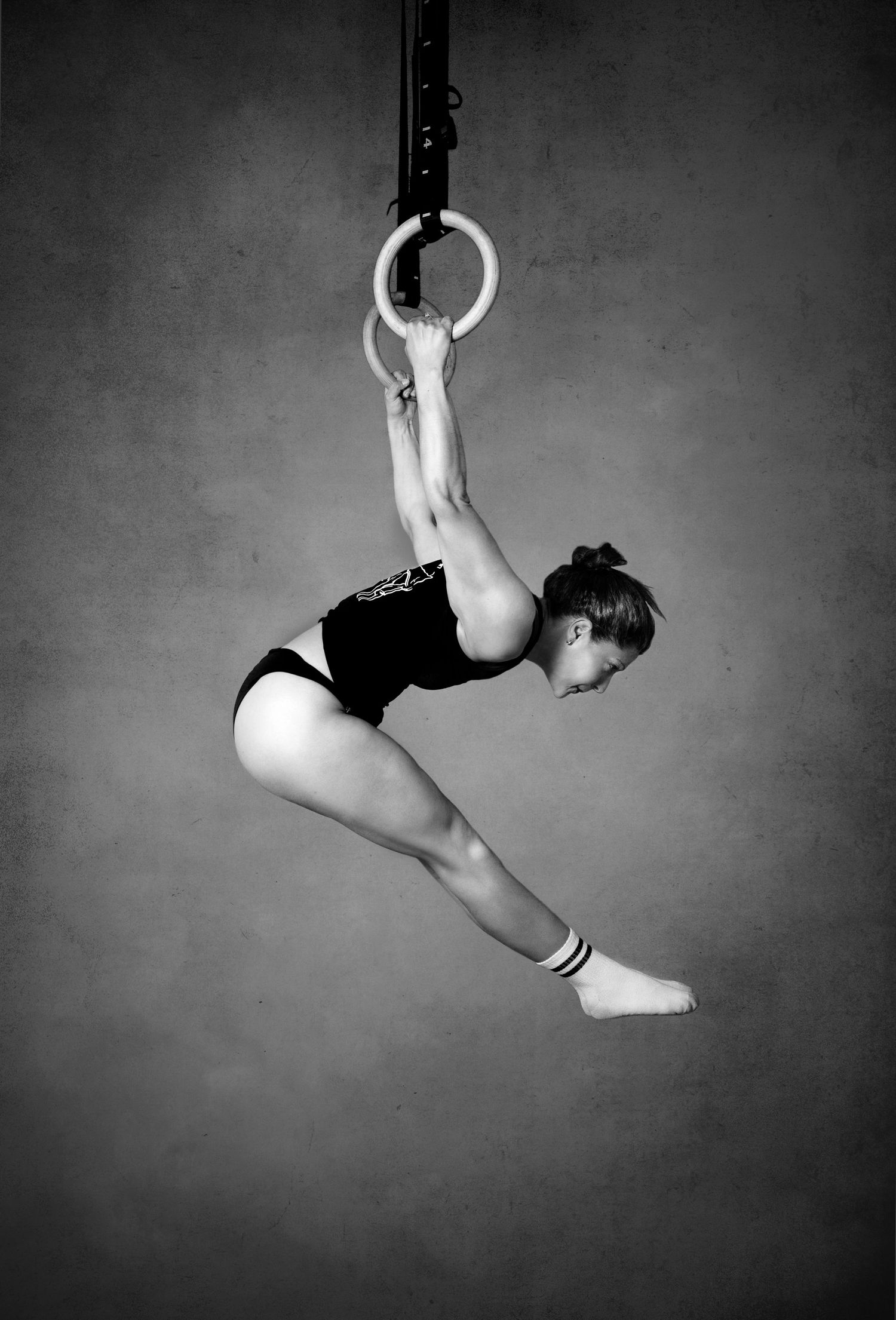 Black and white photograph of a gymnast performing on aerial rings showing strength and grace in a dynamic pose.