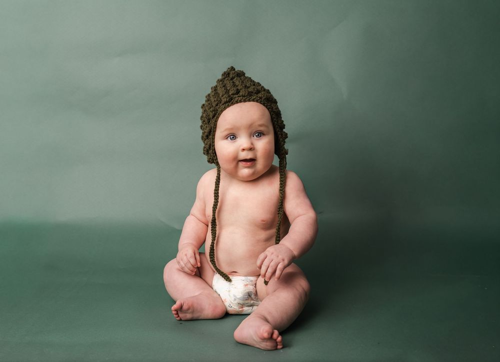 Baby in white diaper poses against green background in series of connected photos showing different positions.