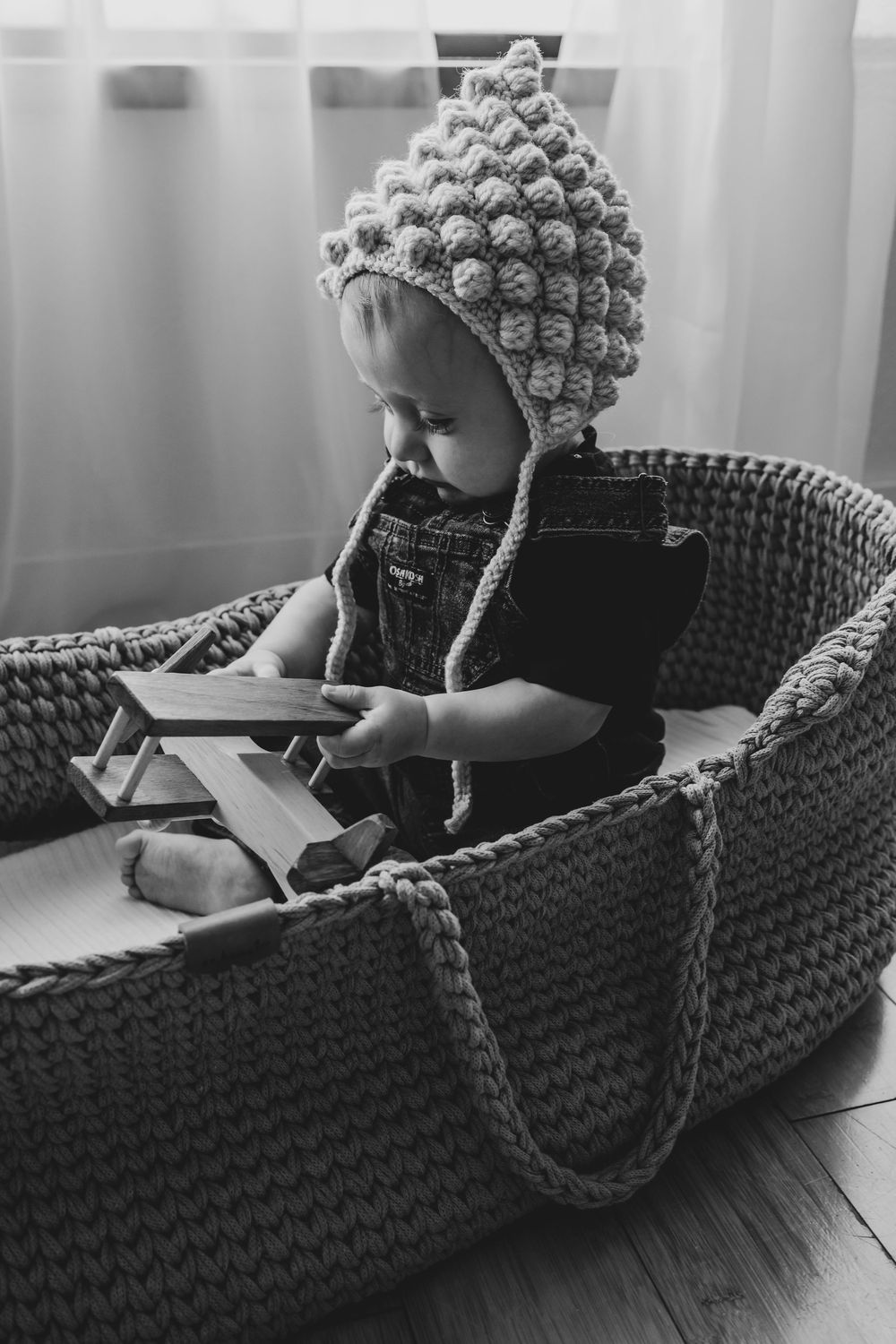 A sequence showing someone in a knit cap working on paper while sitting in a dark woven basket or cradle.