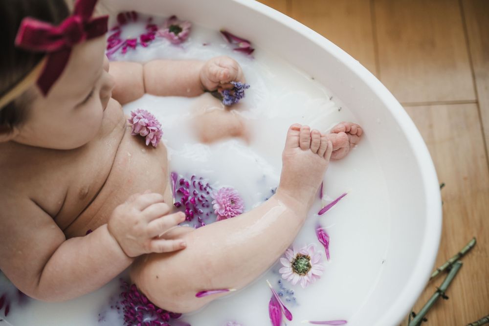 Baby laying in milk bath with floating purple flowers during newborn photography session.