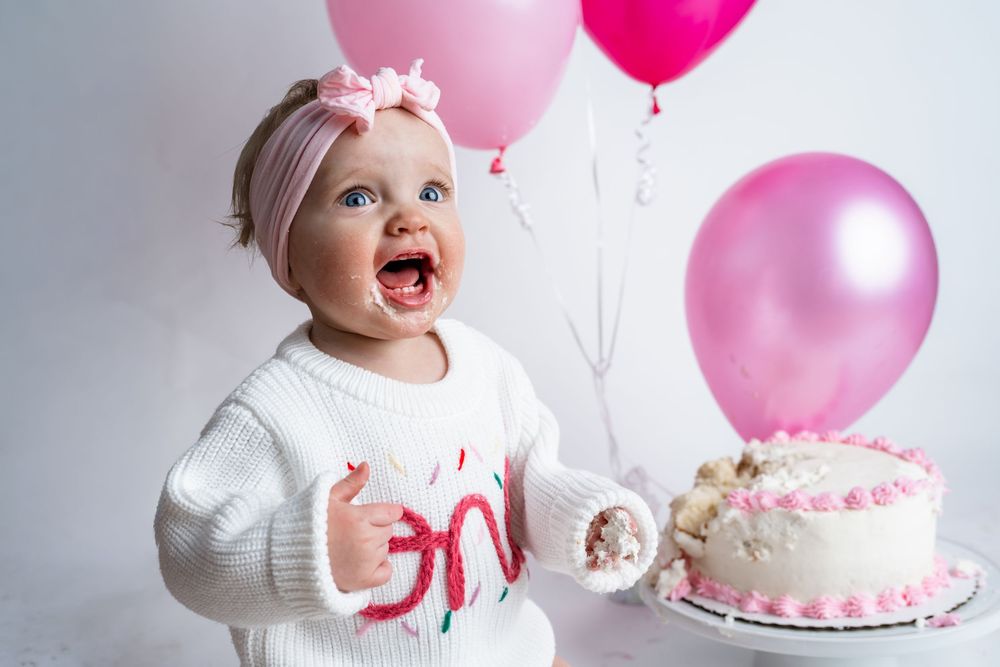 Pink and white birthday party setup with cake and balloons for a first birthday celebration.