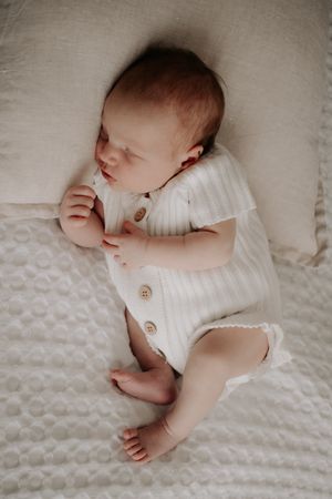 Baby asleep on a cushion on the bed.