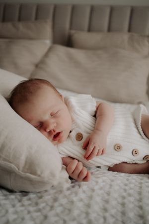 Baby asleep on a cushion on the bed.