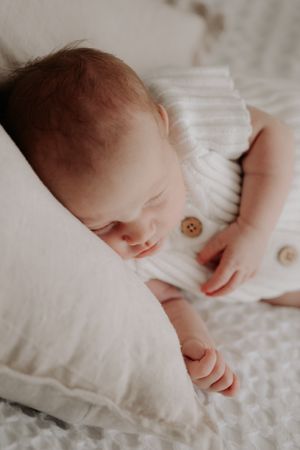 Baby asleep on a cushion on the bed.