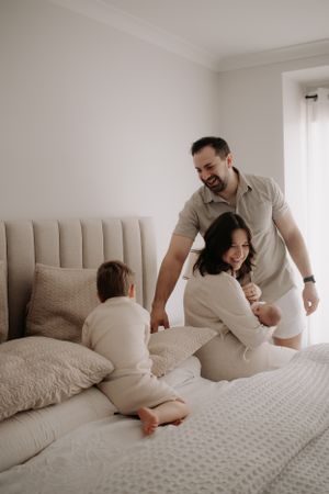 Mum feeding newborn baby on the bed while dad plays with his son.