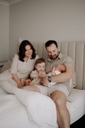Family sitting in their bed looking down at their newborn.