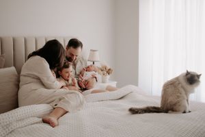 Family sitting in bed with their cat and newborn.