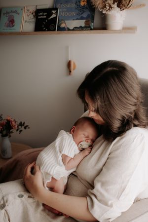 Mum sitting in a nursery holding her sleeping newborn.