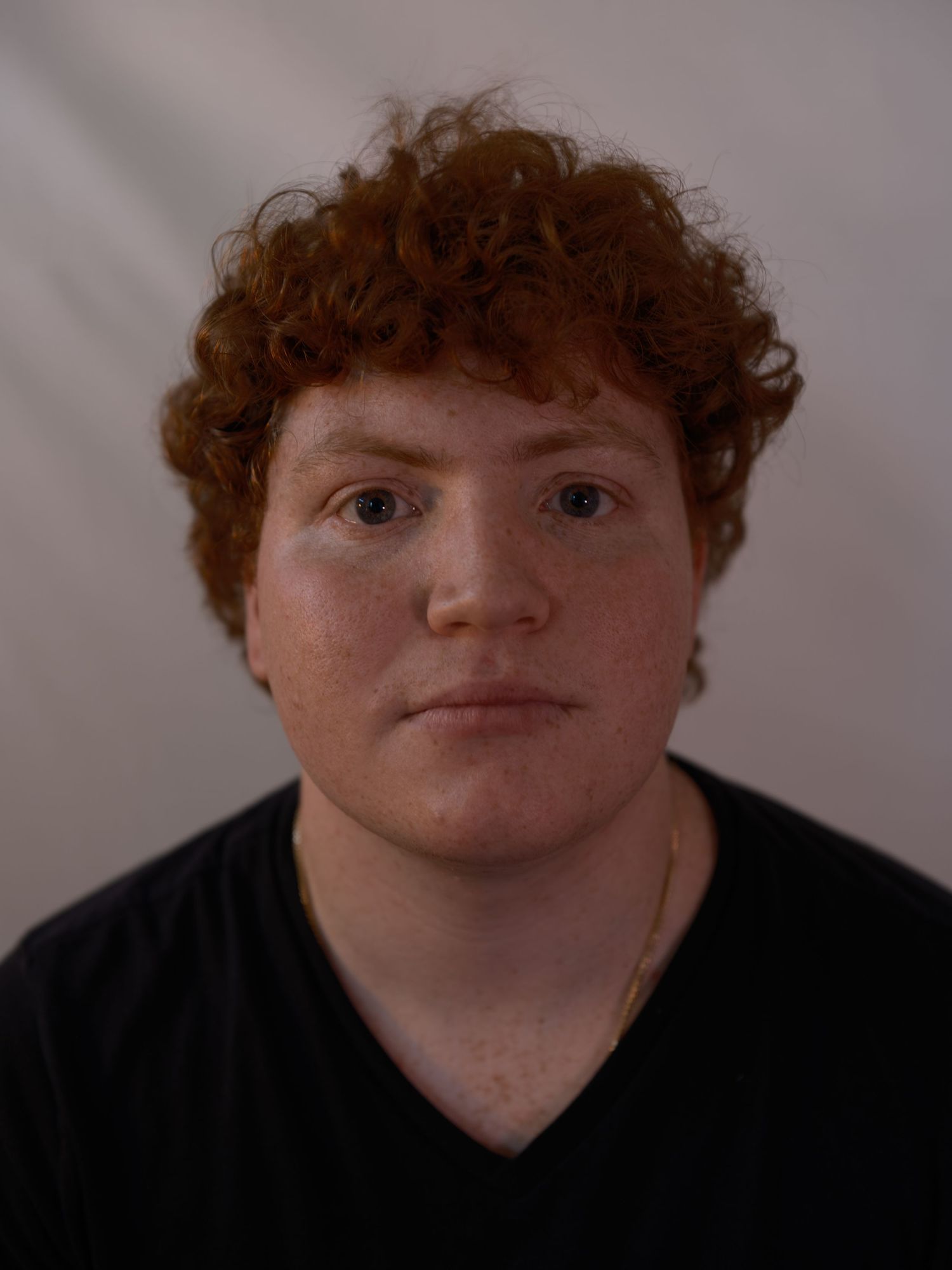 Young person with curly red hair and freckles wearing a black t-shirt against a white background.
