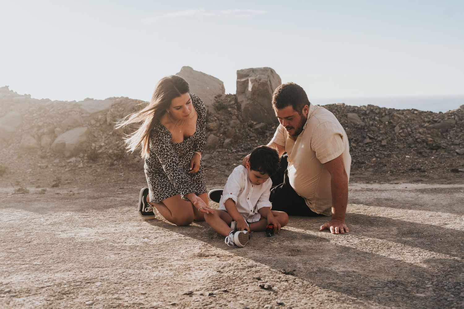 A couple lies on rocky ground during sunset taking photos together in a romantic outdoor setting.