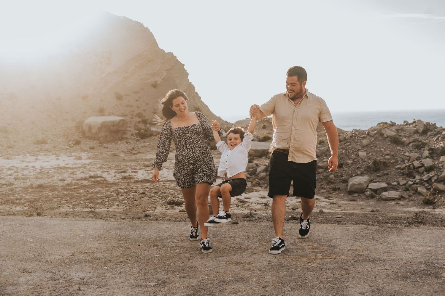 Family walking together on a rocky desert path at sunset, holding hands and enjoying a scenic outdoor adventure.