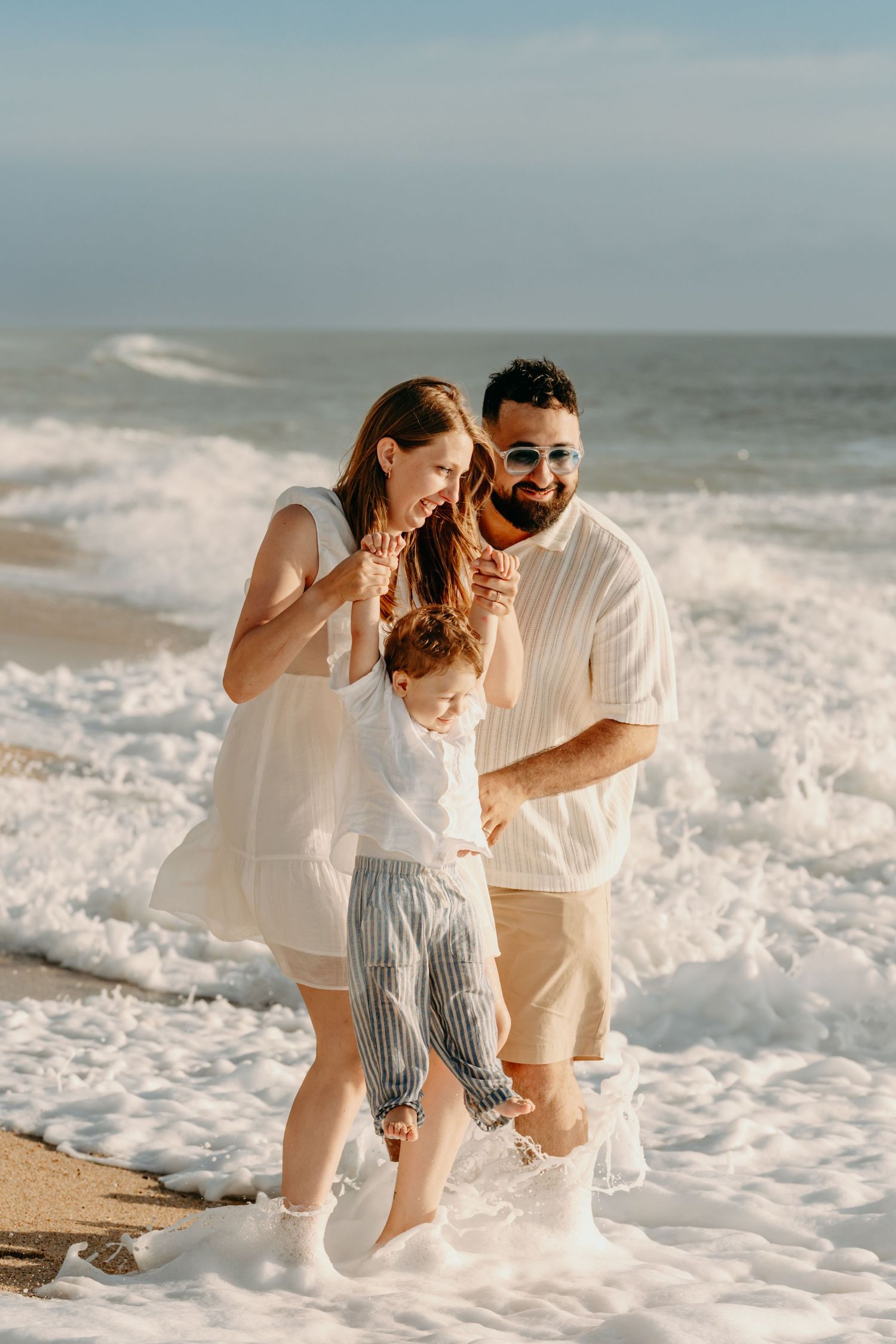 A family plays together on a sunny beach as ocean waves crash at their feet.