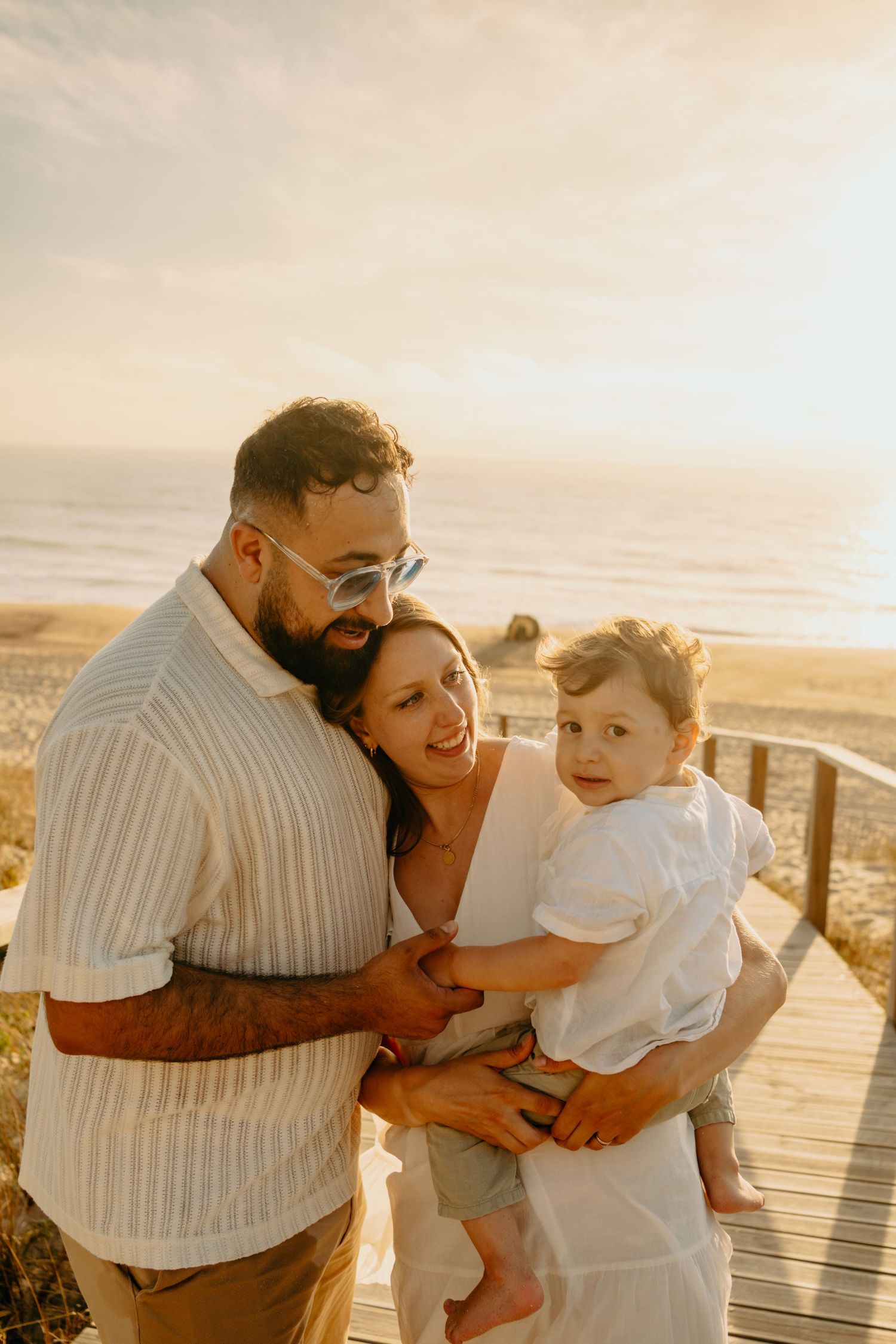 A loving family shares joyful moments together on a wooden boardwalk at sunset by the beach.