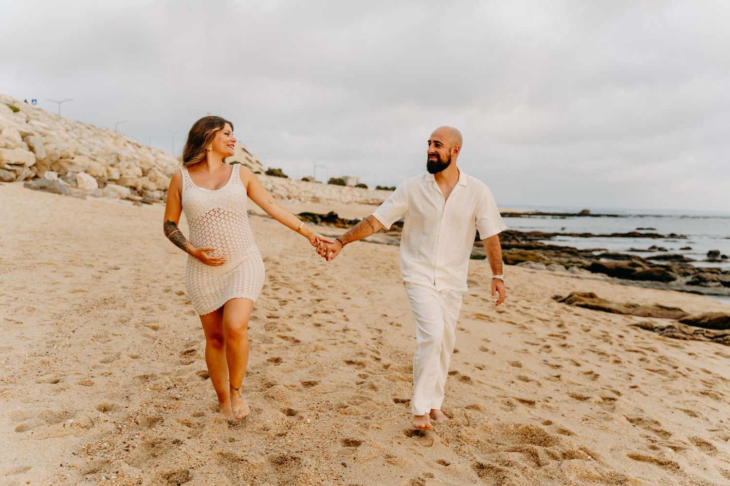 A couple walking and playing together on a sandy beach during sunset with ocean waves in the background.
