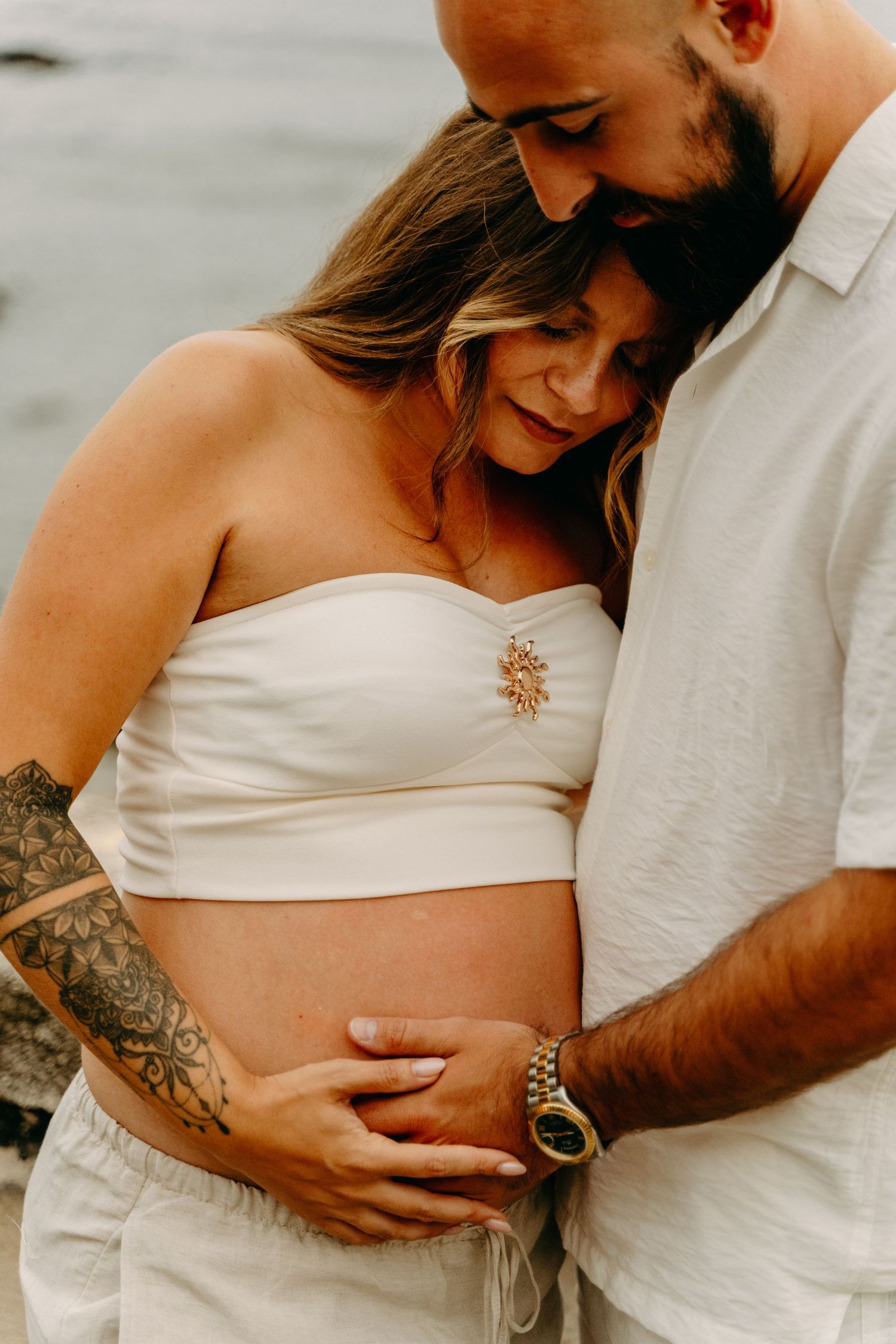 Intimate maternity photoshoot on beach shows couple in white clothing embracing pregnant belly in multiple tender poses.