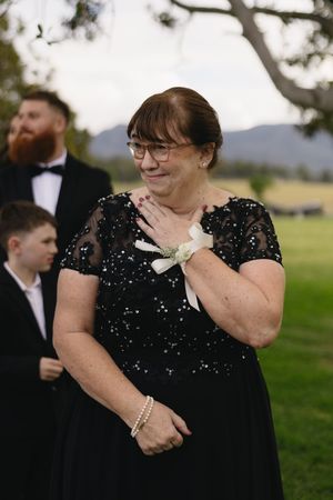 Person in a sparkly black formal dress with glasses and a white corsage stands outdoors at an elegant event.