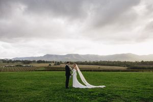 Couple sharing a romantic moment in a green field with mountains and dramatic cloudy skies in the background.